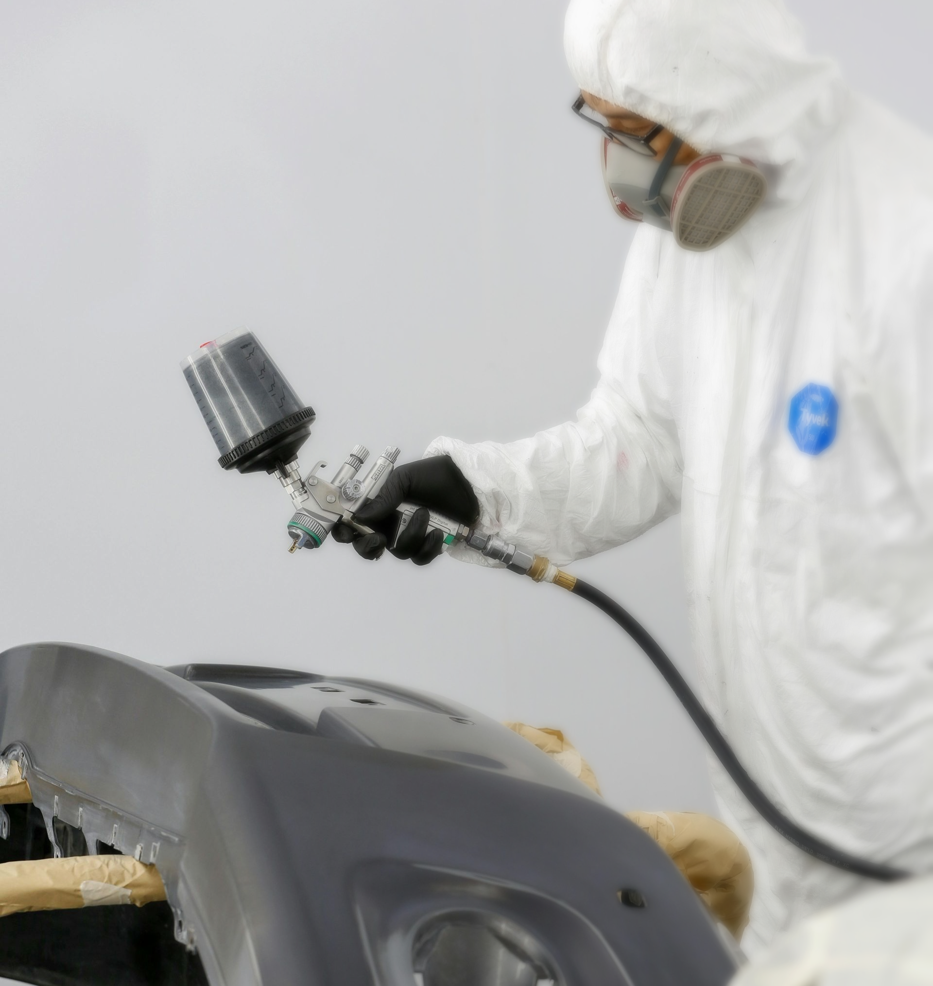 Worker in white protective suit spraying paint onto a black car body with a spray gun