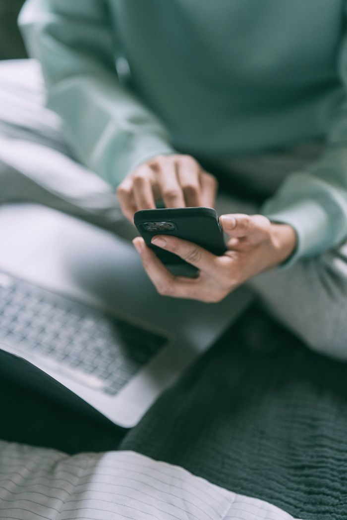 A person is sitting on a bed using a cell phone.