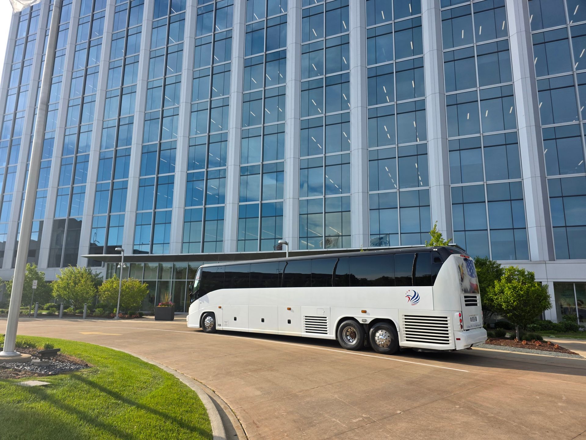 White charter bus parked in front of a modern glass building.