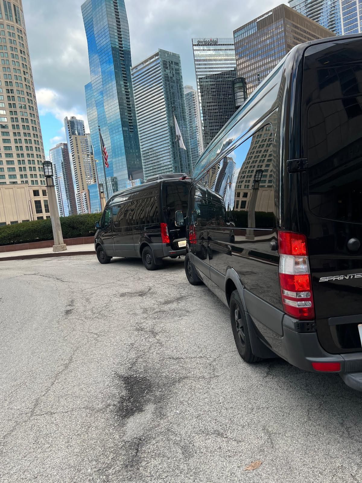Two black vans parked on a city street, tall buildings in the background.