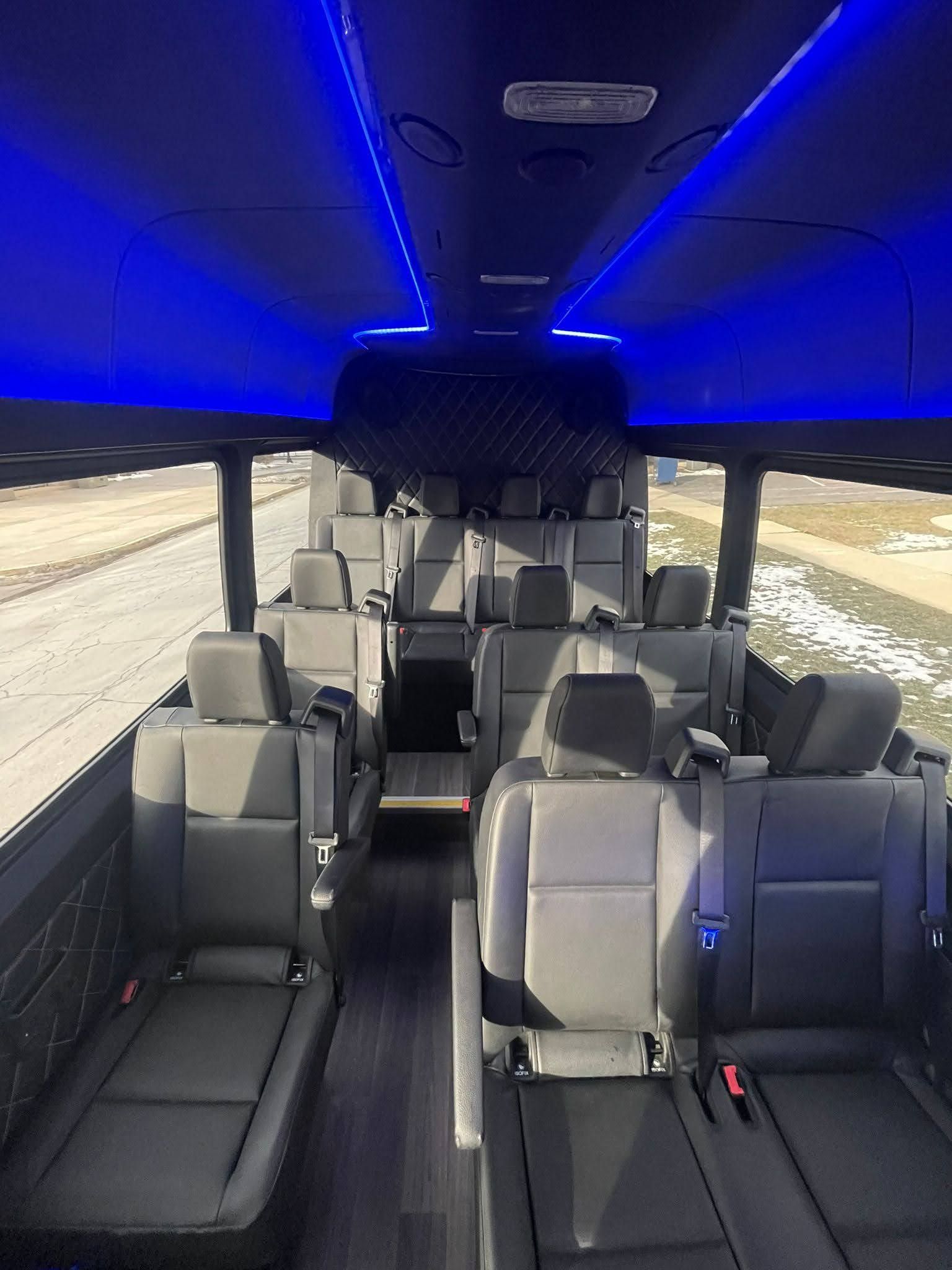 Interior view of a passenger bus with gray seats, blue overhead lights, and a dark ceiling.