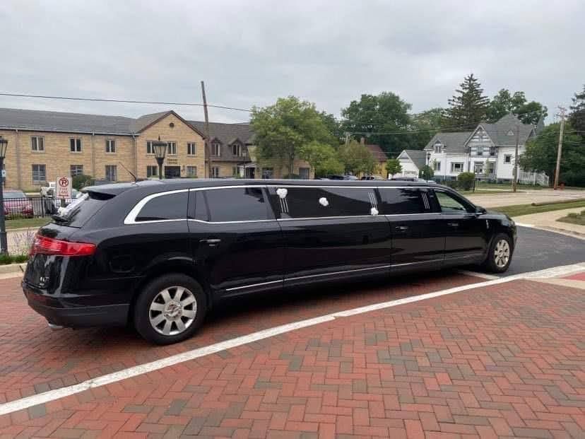 Black limousine on a brick street near buildings and trees on a cloudy day.