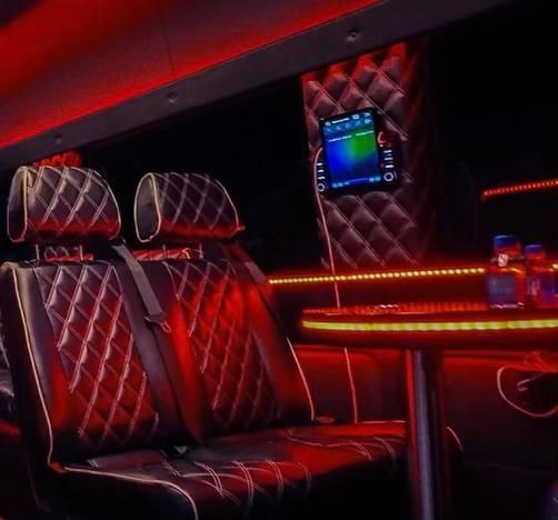 Black leather interior of a van, diamond-stitched seats, red LED lighting, and a tablet on the wall.