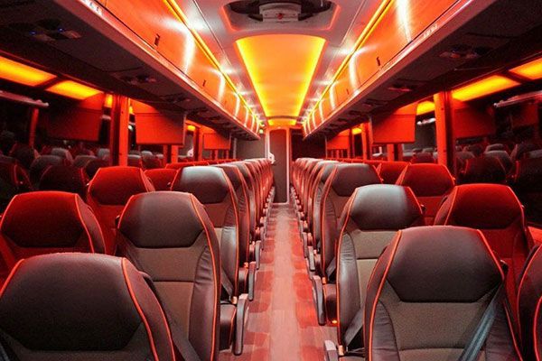 Interior of a bus, with rows of dark seats, and orange interior lighting.