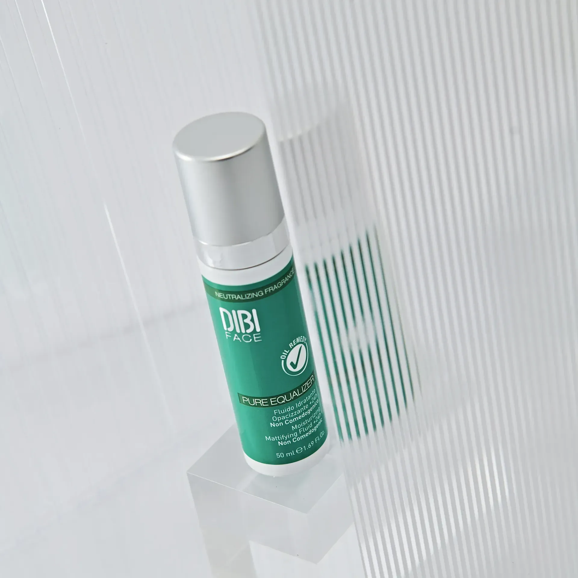 Flacone verde e argento del prodotto DIBI Milano su un supporto trasparente su uno sfondo bianco con linee verticali.