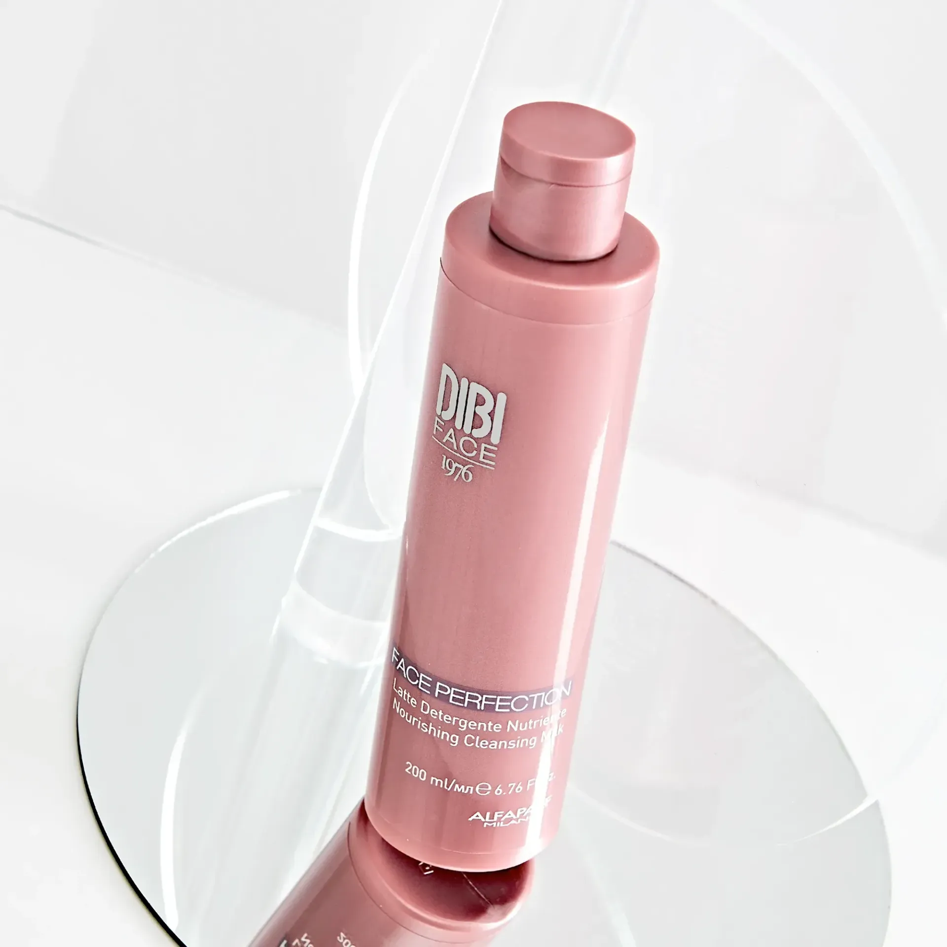 Flacone rosa di prodotto per la cura della pelle Dibi Milano su una superficie riflettente.