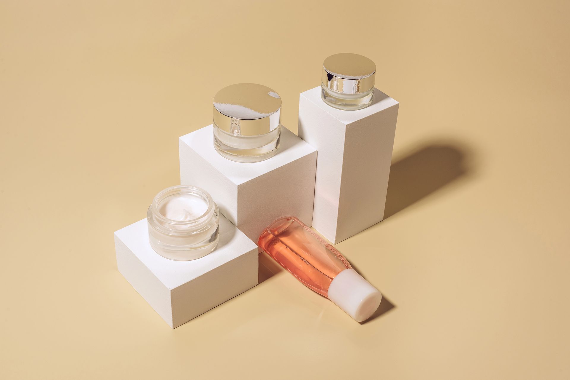 Barattoli e tubetti di cosmetici su blocchi bianchi su sfondo beige.