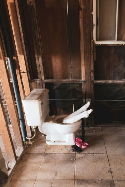 White toilet tipped in a damaged wooden room, with a pink item on the floor.