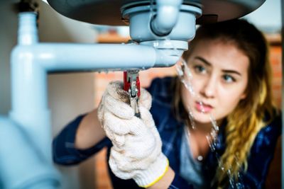 Person wearing gloves repairs a sink pipe under a bathroom basin