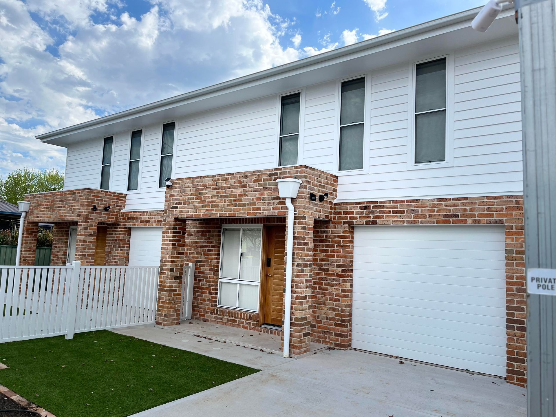 White and brick townhouses with a garage, front door, and small lawn.