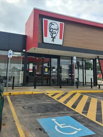 Exterior of a KFC restaurant with accessible parking. Red and white logo above glass doors.