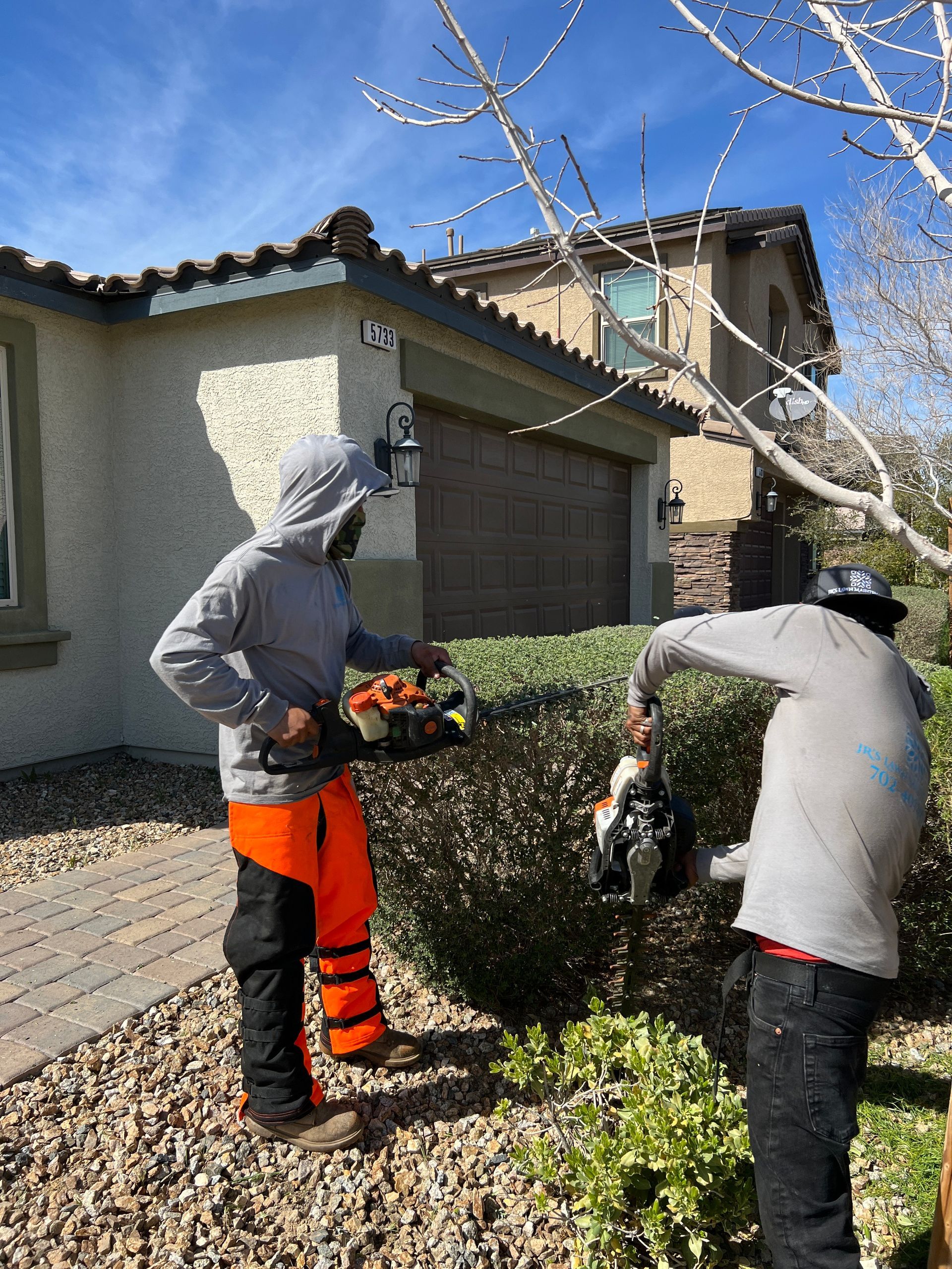 two men are cutting a hedge in front of a house .