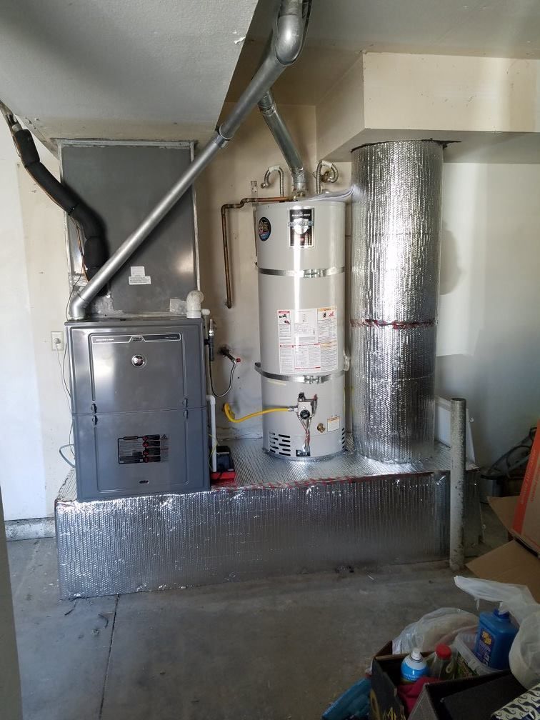 Furnace and water heater in a utility room, silver metal, insulated pipes, gray and beige walls.