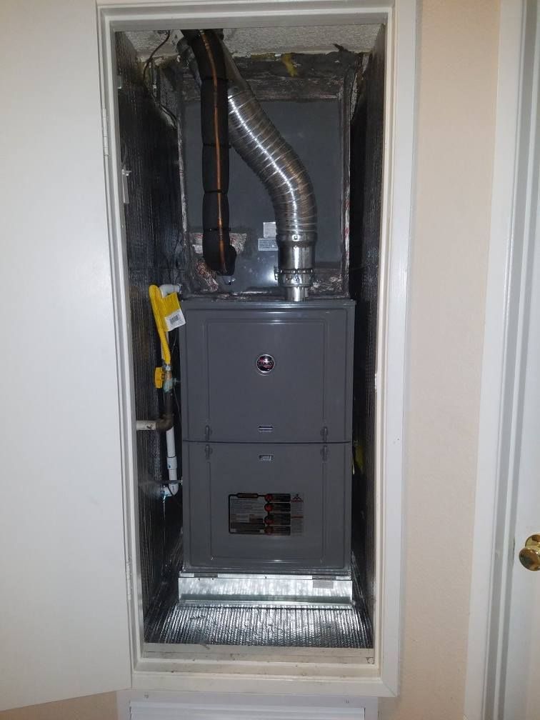 A furnace unit housed in a closet, with vent pipes and wiring visible.