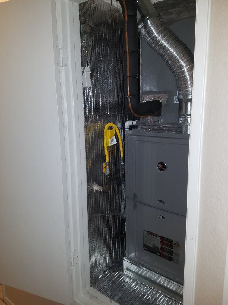 Furnace in a utility closet with insulated walls; a yellow cord hangs down.