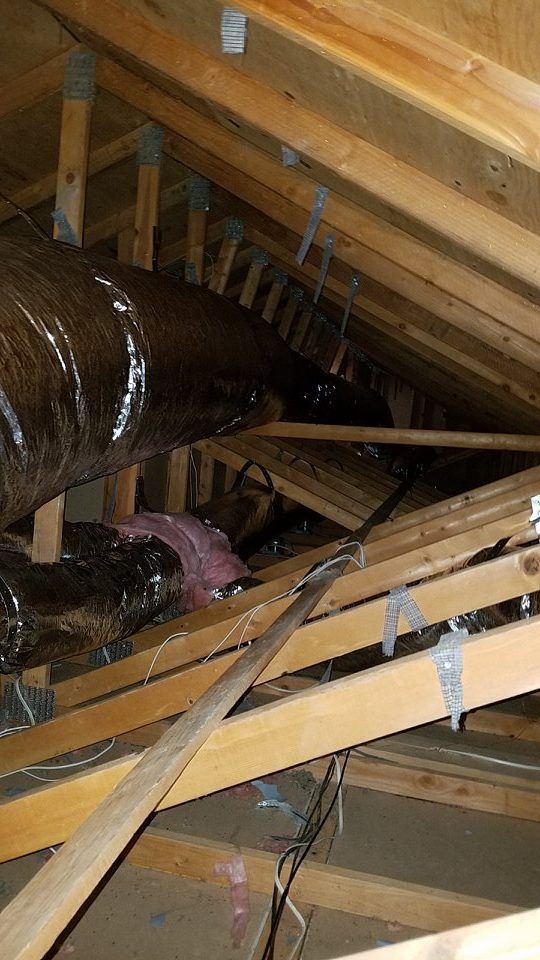 View of an attic with ductwork, wooden beams, and some wires, angled upwards.