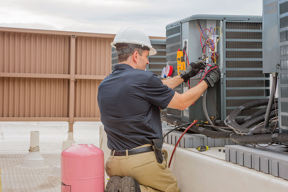 HVAC technician in a hard hat working on an air conditioning unit on a rooftop.