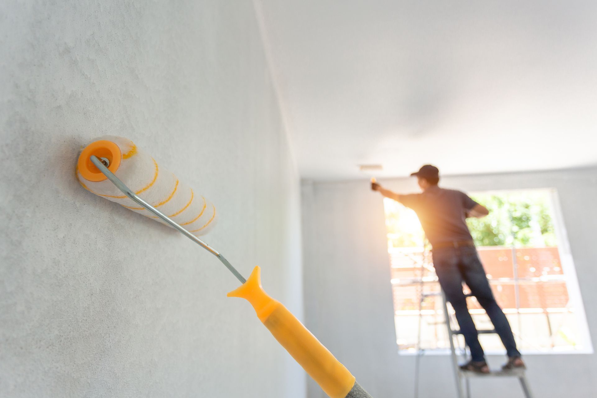 A man is standing on a ladder painting a wall with a paint roller.