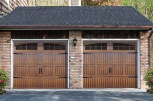 A brick garage with two wooden garage doors and a black roof.
