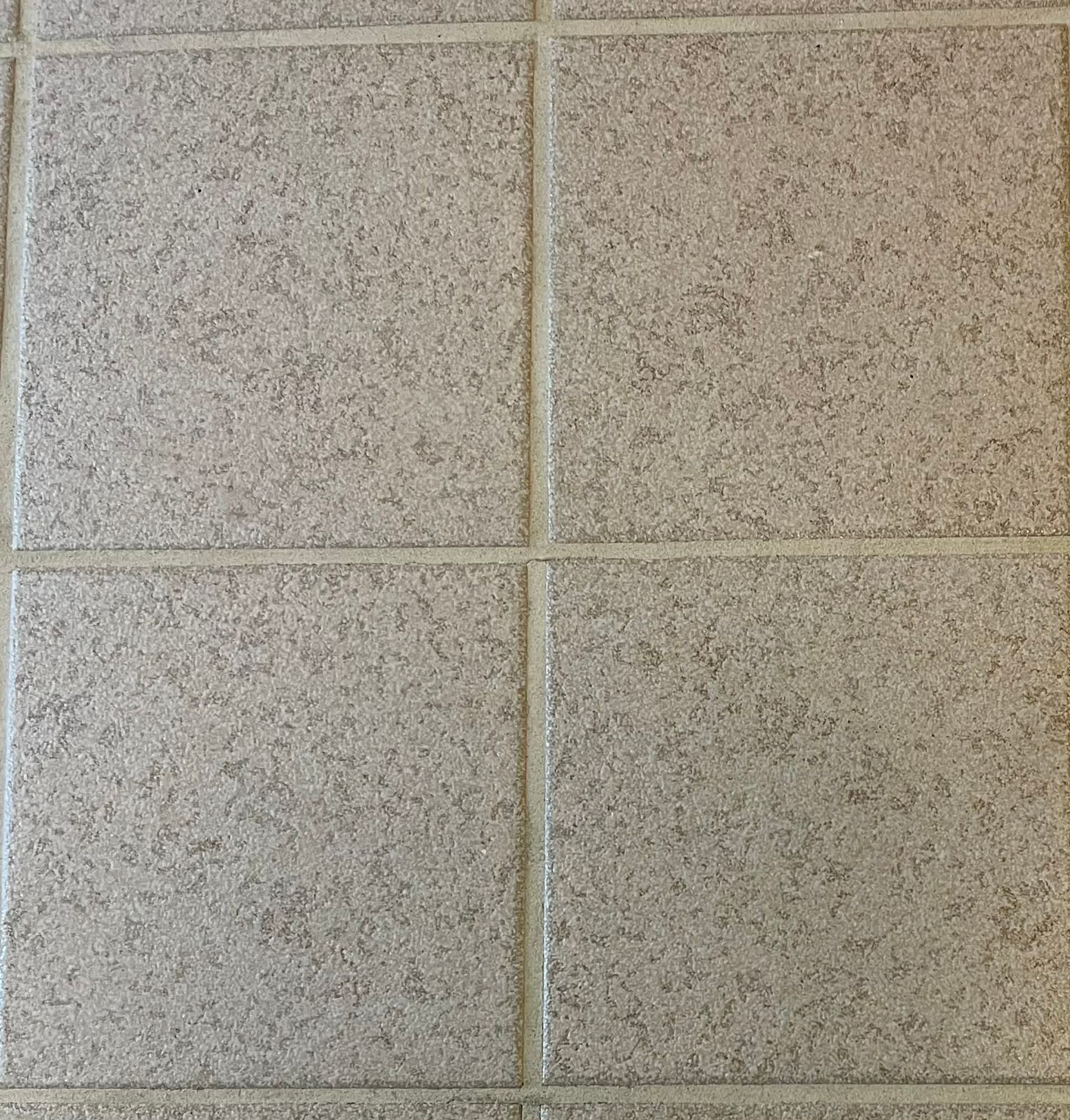Close-up of four beige speckled floor tiles with grout lines forming a cross.