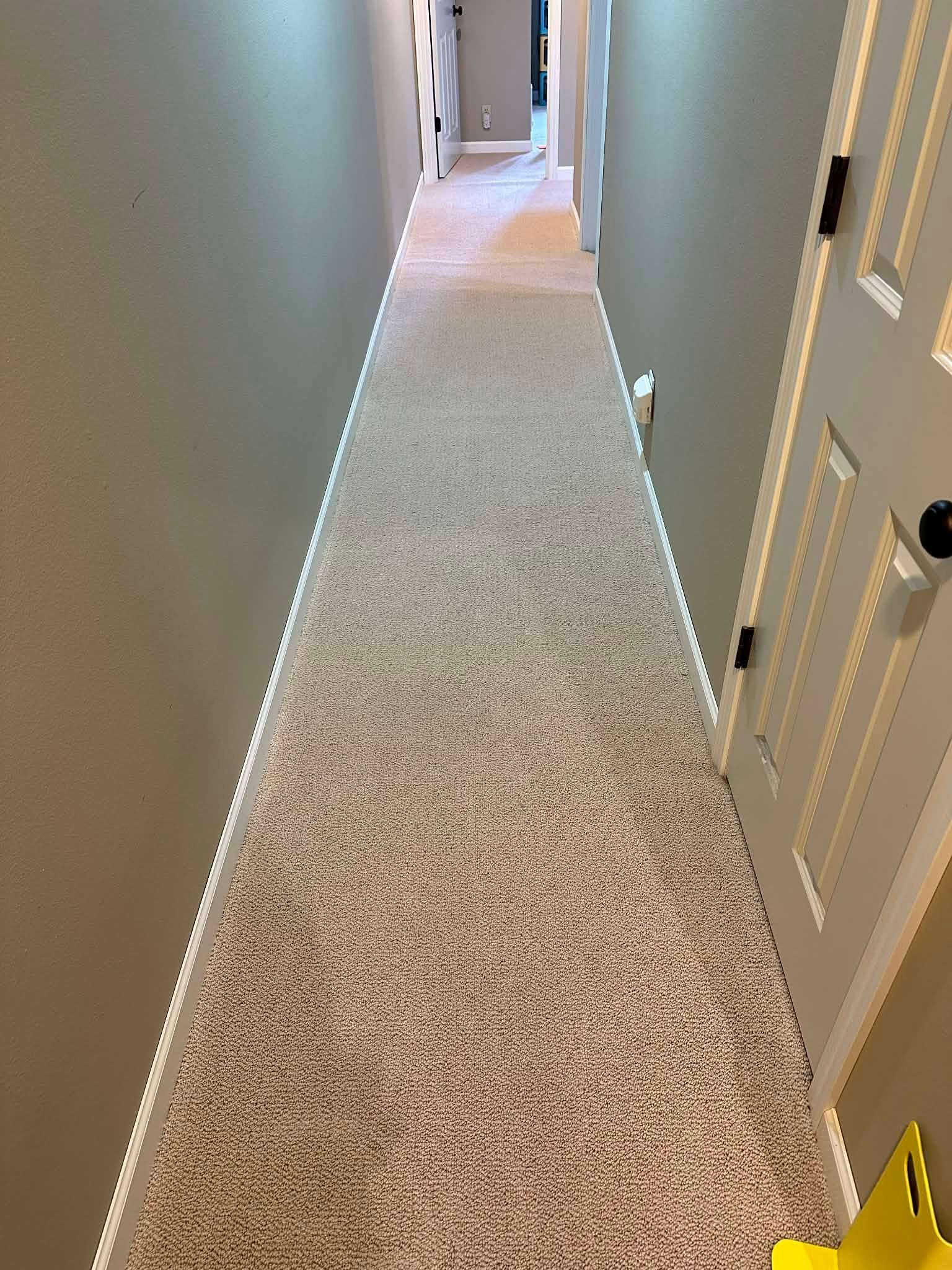 Carpeted hallway with white doors and beige walls, viewed from one end looking down the narrow corridor.