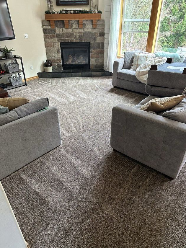 Living room with stone fireplace, light gray sofas, and a carpeted floor by a large window.