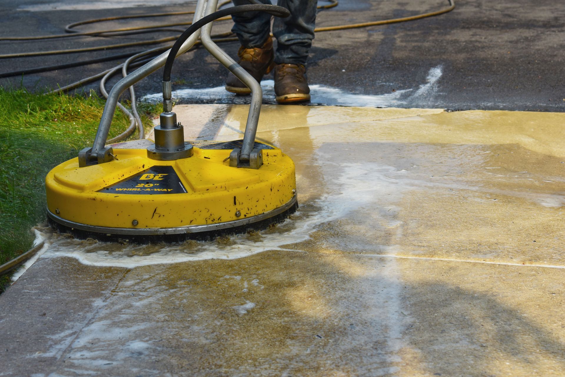 A person is using a yellow machine to clean a concrete driveway.