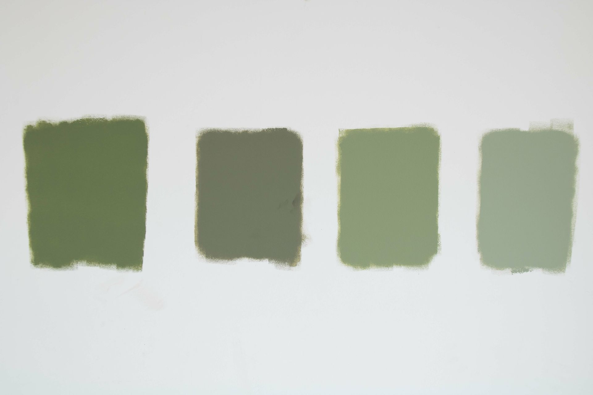 Four different shades of green paint are lined up on a white surface.