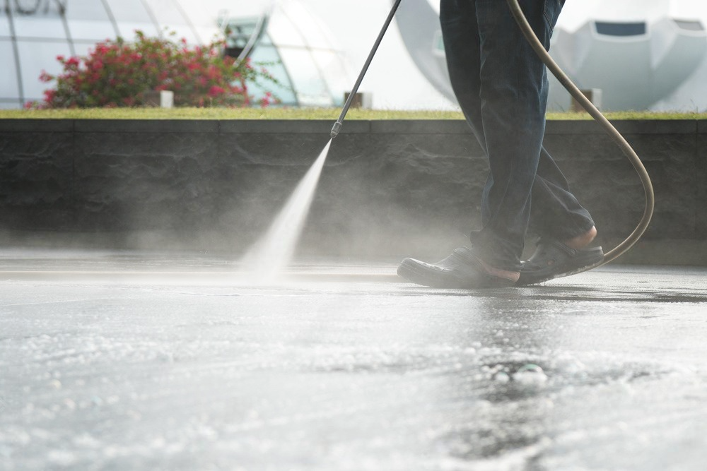 A person is using a high pressure washer to clean a concrete surface.