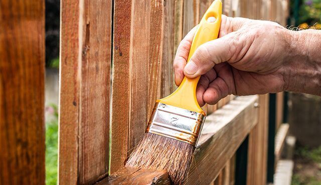 A person is painting a wooden fence with a brush.