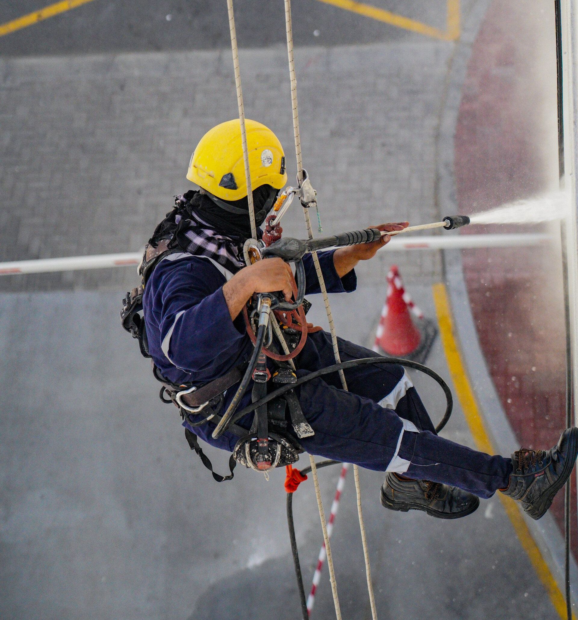 A man wearing a yellow helmet is spraying water on a building