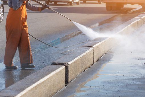 A man is using a high pressure washer to clean the sidewalk.