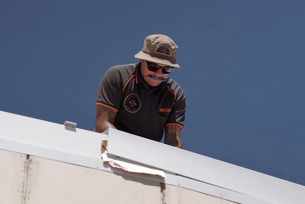 An Electrician Wearing A Hat And Sunglasses Is Working On A Roof — Entire Trades in Port Stephens, NSW