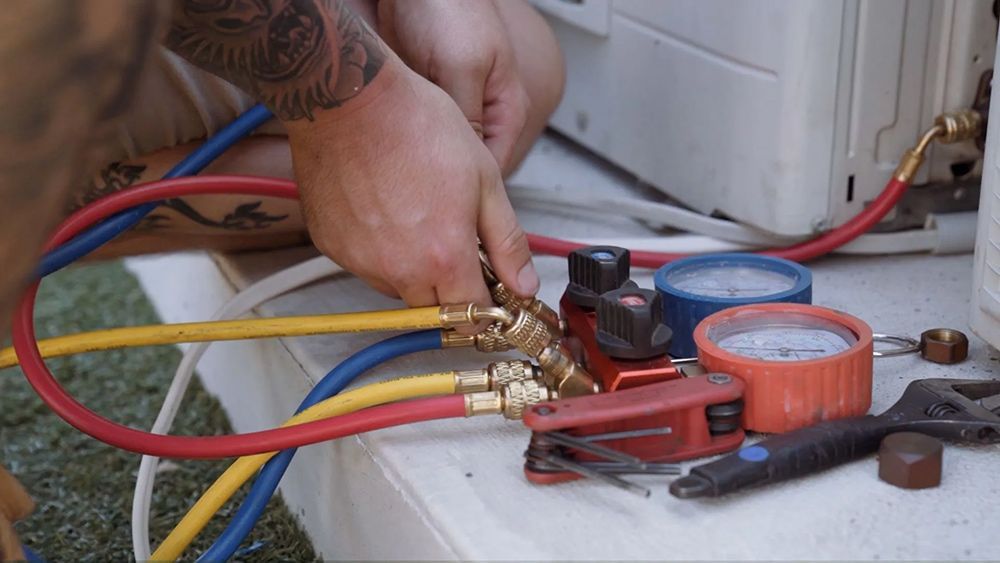 A Man Is Working On An Air Conditioner With Hose And Gauges — Entire Trades in Port Stephens, NSW