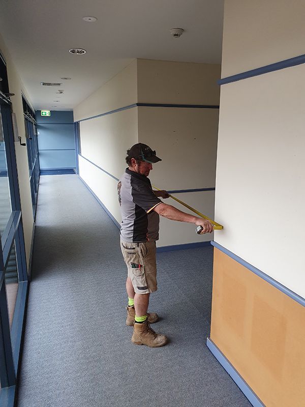 A Man Is Measuring A Wall With A Tape Measure — Entire Trades in Port Stephens, NSW