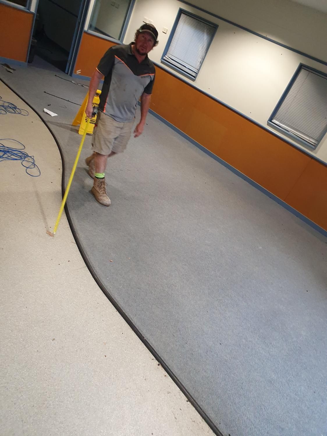 A Man Is Measuring a Curved Carpet with A Tape Measure — Entire Trades in Singleton, NSW