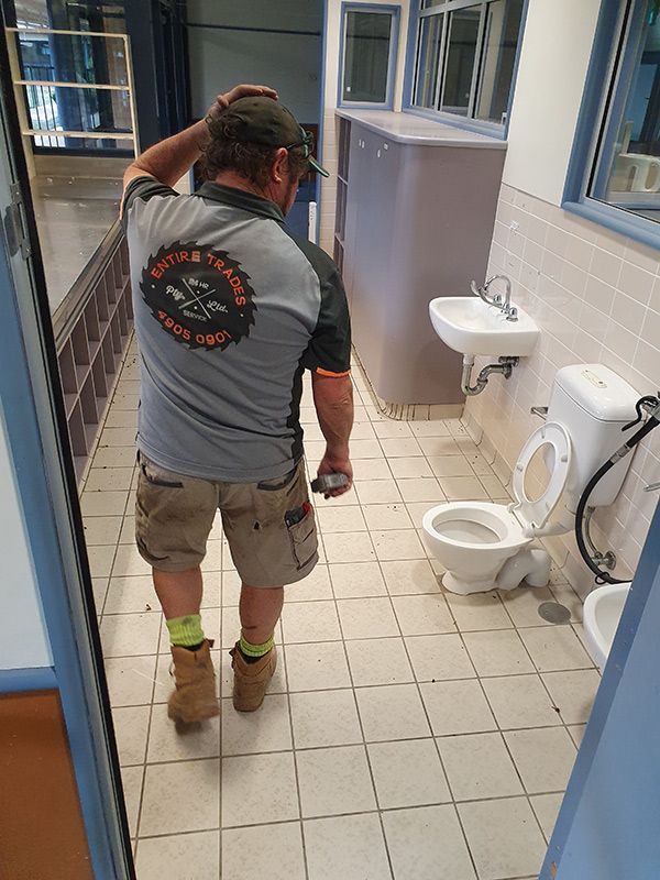 A Carpenter Man Wearing An Entire Trades Shirt Walks Through A Bathroom With Toilet And Cabinets — Entire Trades in Port Stephens, NSW