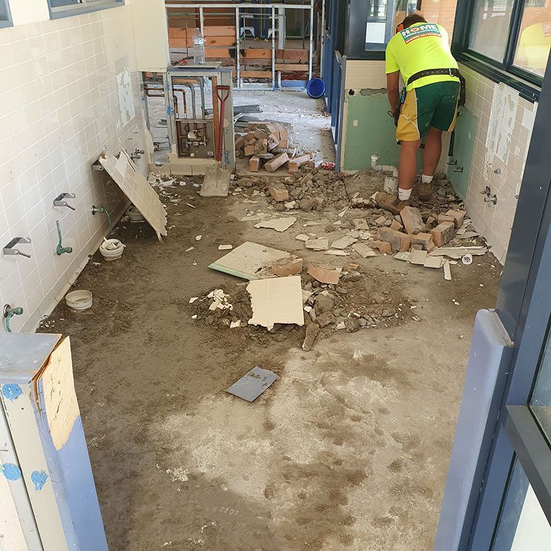 A Man Working on Demolishing Bathroom Tiles in a Building Construction — Entire Trades in Cessnock, NSW