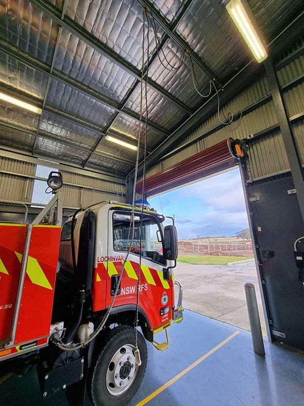 A Red And Yellow Fire Truck Is Parked In A Warehouse With The Door Open And Lights Installation — Entire Trades in Cessnock, NSW