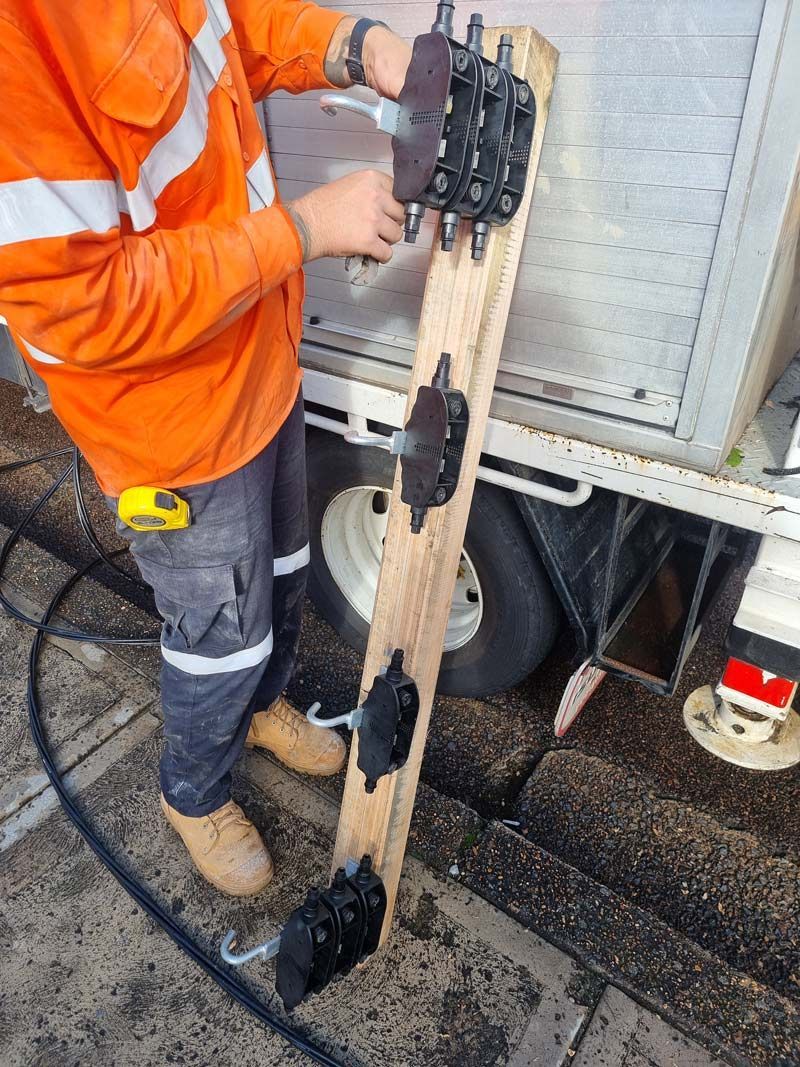 A Man In An Orange Shirt Is Working On A Piece Of Wood And Power Line Cable Platform — Entire Trades in Maitland, NSW