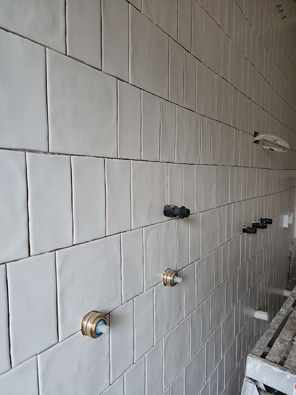 A Bathroom Wall With White Tiles And Brass Faucets — Entire Trades in Central Coast, NSW
