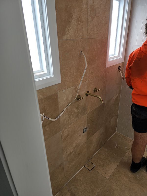 A Man Wearing An Orange Shirt Stands In A Bathroom Under Construction — Entire Trades in Singleton, NSW