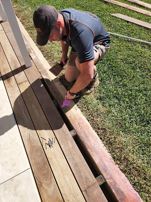 A Man Is Working On A Wooden Deck In The Grass — Entire Trades in Central Coast, NSW