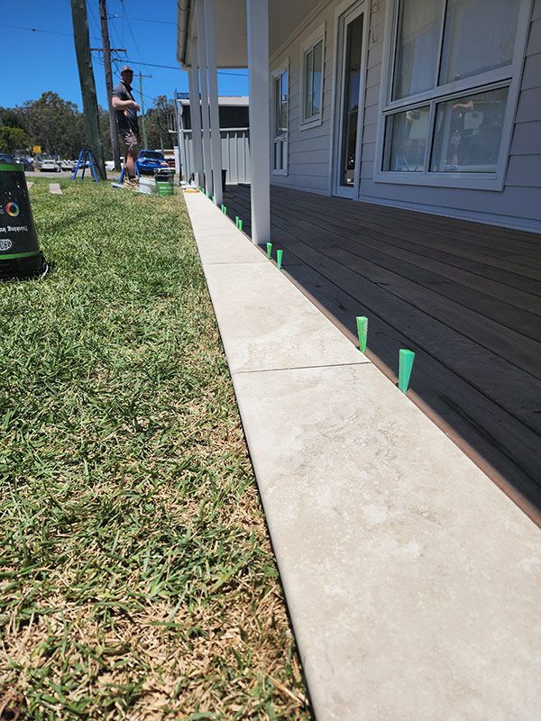 A Man Standing On A Sidewalk Next To A House With Wooden Deck — Entire Trades in Singleton, NSW