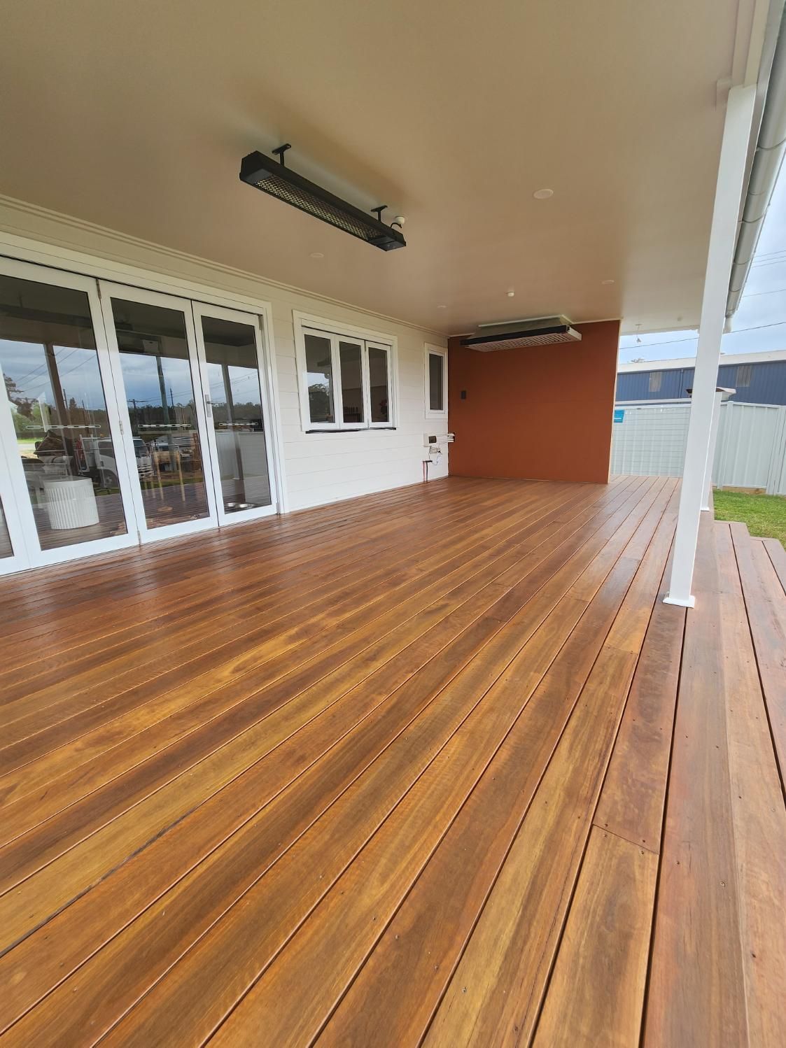A Large Wooden Deck with A White Roof and Sliding Glass Doors — Entire Trades in Maitland, NSW