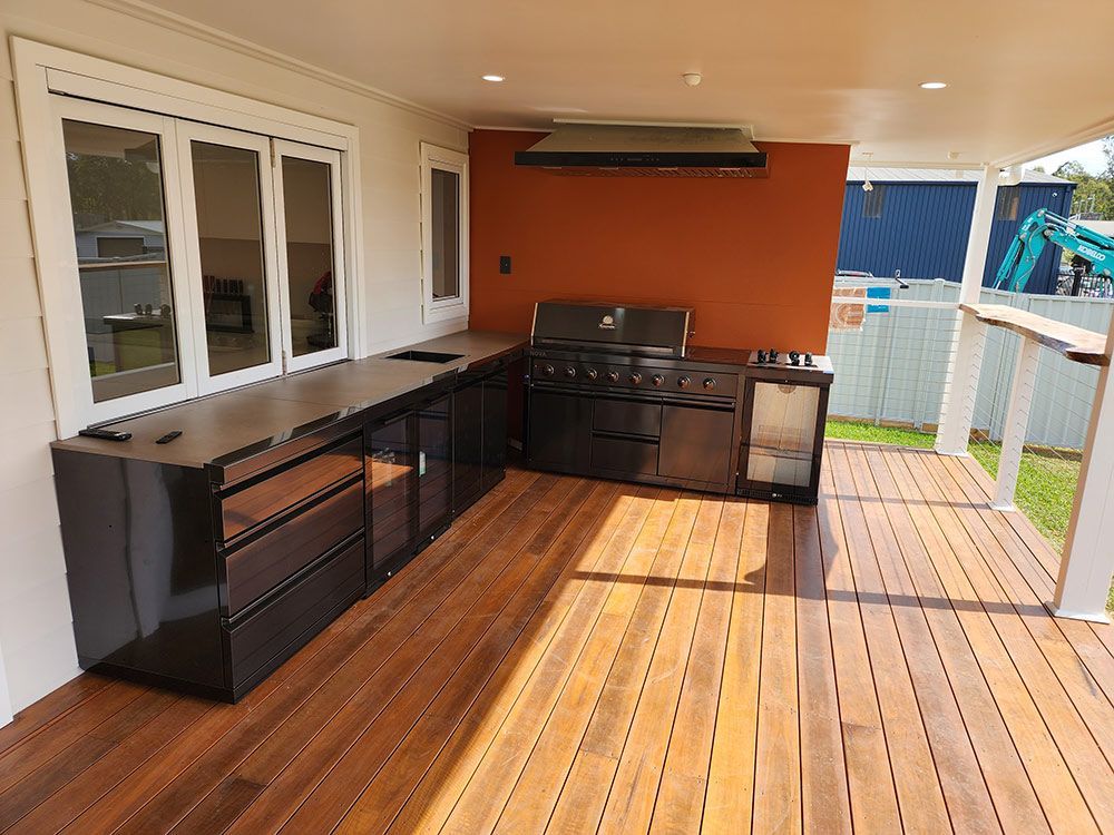 Outdoor Kitchen With Black Cabinet And Wooden Deck — Entire Trades in Central Coast, NSW