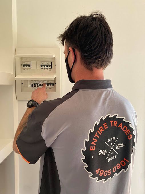 A Man Wearing A Mask Is Working On An Electrical Box — Entire Trades in Singleton, NSW
