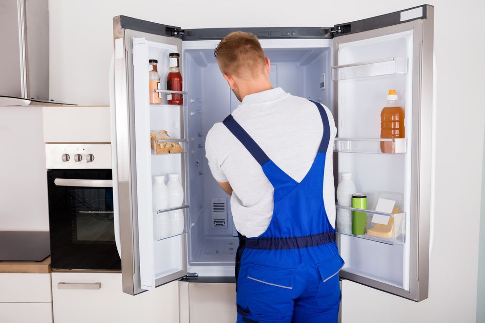 Repairman In Blue Uniform Fixing Refrigerator Cabinets — Entire Trades in Cessnock, NSW