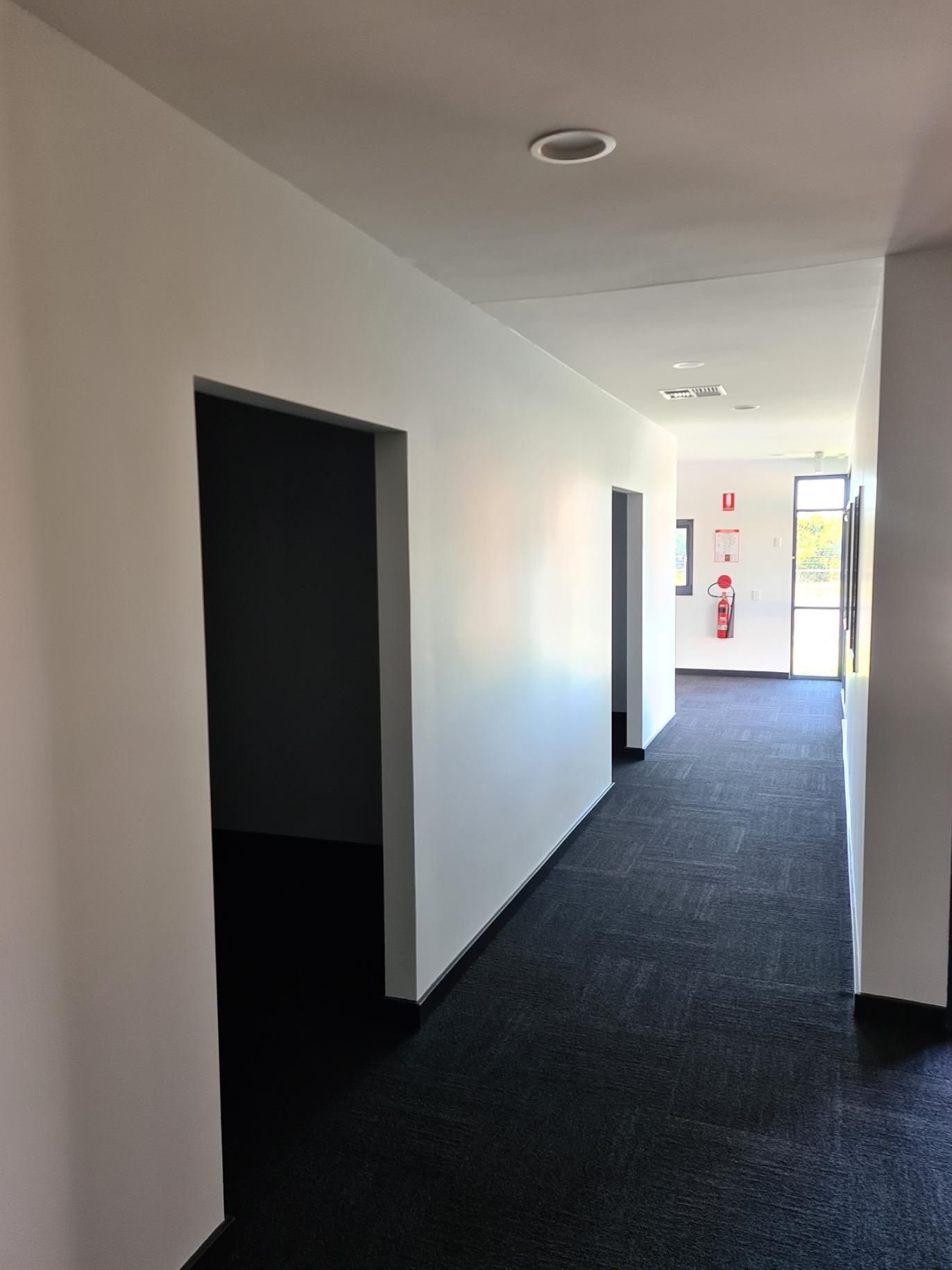 A Long Hallway with Black Carpet and White Walls in An Office Building — Entire Trades in Maitland, NSW
