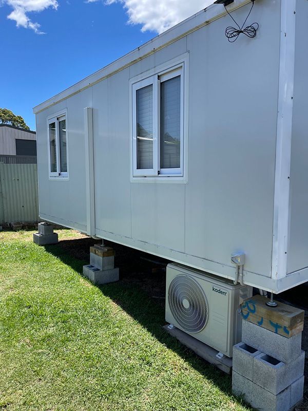 A White House With A Window And An Air Conditioner Is Sitting On Top Of A Lush Green Field — Entire Trades in Maitland, NSW